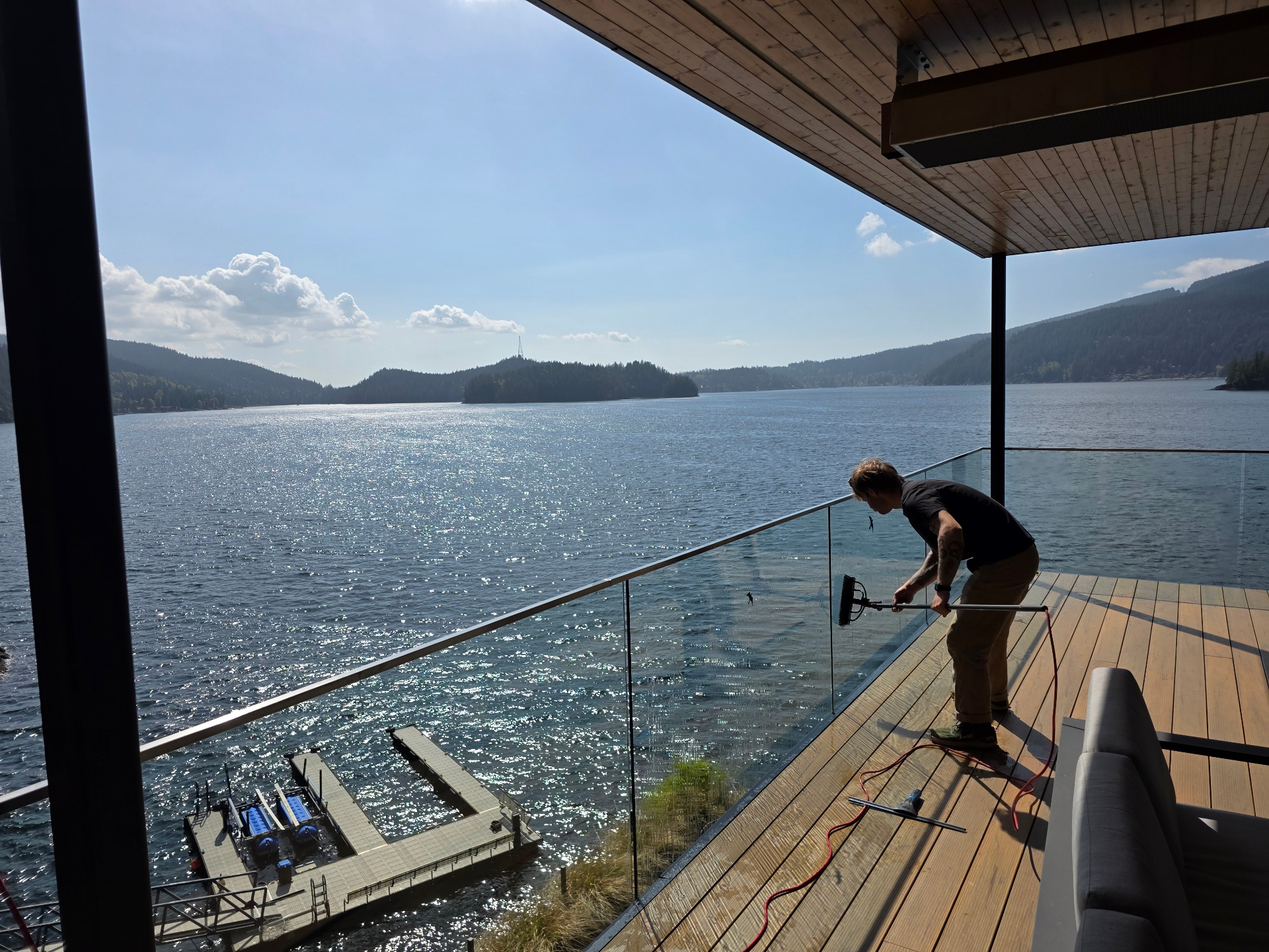 Complete Window Cleaning technician detailing glass railings on a sunlit waterfront deck overlooking the Indian Arm inlet
